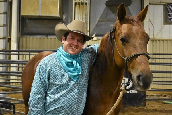 male student wearing cowboy hat with his arm draped across his horse